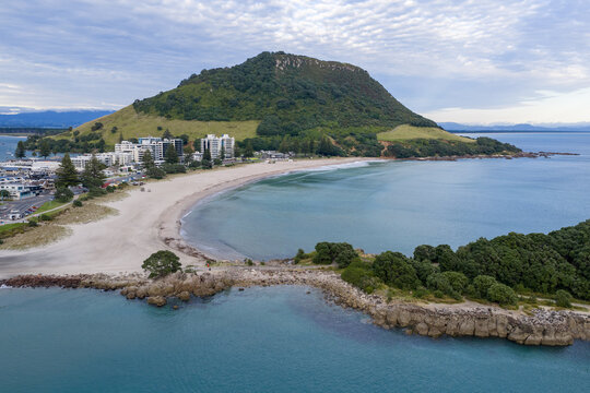 Aerial view of the majestic Mount Maunganui standing tall, its lush green slopes meeting the turquoise waters of the ocean, Tauranga, New Zealand.