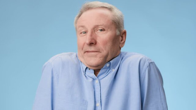 A man in a blue shirt appears unsure or puzzled while standing in front of a light blue background. His facial expression shows confusion. The footage captures a light moment.
