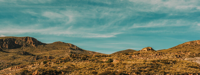 Arid rocky rough landscape with some vegetation and trees under a blue sky with some clouds. Huebro, Almeria, Andalusia, Spain. © ysbrandcosijn