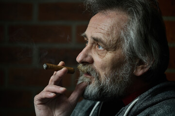 Senior bearded man smoking on balcony classic big cigar in detail