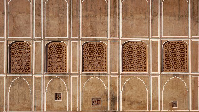 Traditional Indian palace wall with arched windows and detailed jaali lattice design, showcasing heritage architecture and geometric patterns.