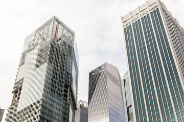 In a bustling city center, several skyscrapers reach high into the sky. Their glass exteriors reflect the light as people go about their day below