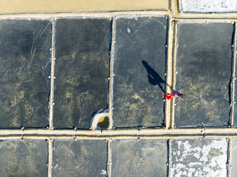 Aerial view of a person walking across salt pans with striking contrasts of light and shadow reflecting the sky, Cox's Bazar, Bangladesh.