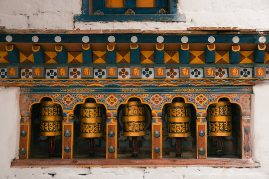 Paro, Bhutan - 16 September 2025: View of prayer wheels set against a white stone wall, adorned with intricate blue, yellow, and red patterns, creating a vibrant tapestry of cultural artistry.