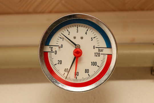 A round analog manometer in a metal case displays pressure and temperature readings in the system using contrasting black and red hands.