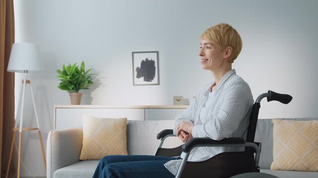 A woman sits in a wheelchair, facing forward in a well-lit room. The space includes plants and soft furnishings. Natural light fills the area, creating an inviting atmosphere.