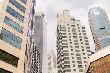 Obraz premium Tall buildings stand side by side in a busy city area. The structures reflect modern design with glass facades and varied heights. The sky is filled with clouds