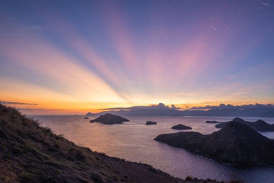 View of the sun's radiant rays burst across the sky, illuminating the islands and sea in a serene, colorful symphony, West Manggarai Regency, Indonesia.