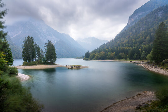 View of tranquil waters mirroring the brooding sky, framed by the rugged embrace of the Julian Alps and lush forests, Trentino, Friuli-Venezia Giulia, Italy.