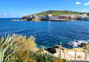 View of Marsalforn with agaves, rocks and turquoise sea under blue sky
