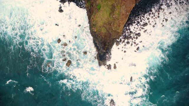 Aerial top down view of a sharp rock cliff edge with crashing ocean waves, drone flying backwards revealing Atlantic blue water and white foam at Miradouro do Guindaste in Madeira island coast.