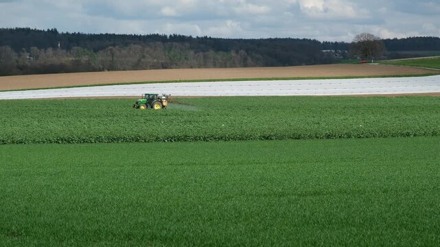 Traktor spr&uuml;ht Pflanzenschutzmittel im Fr&uuml;hling auf dem Feld in der Schweiz, Ackerbau im Monat M&auml;rz