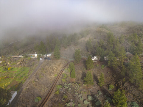 Aerial view of a train track cutting through a rugged landscape, with low-hanging clouds obscuring the peaks, El Teide, Tenerife, Canary islands, Spain.