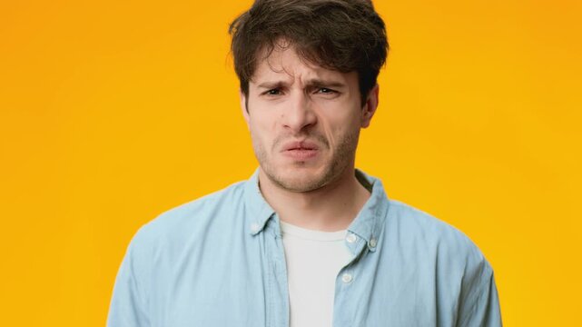 A young man is standing against a bright orange background. He shows a puzzled expression as he looks directly at the camera. The setting is casual and filmed in high resolution.