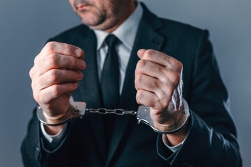 Close-up of arrested businessman in suit wearing handcuffs, symbolizing crime, corruption, fraud, and legal consequences in corporate and financial environments.