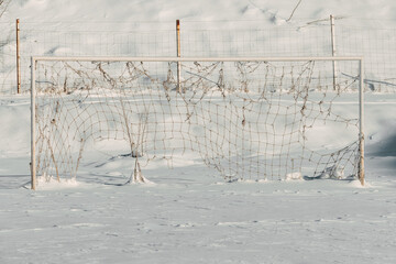 Old white soccer goal frame and sagging net completely covered in frost and snow, standing in a vast snowy field