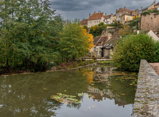 Fototapeta premium Semur-En-Auxois, France - 10 21 2025: Panoramic view of the rampart, old city reflecting on the water with autumn colors from bottom along Armancon river
