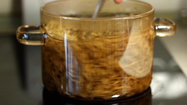 A cook prepares millet and oats on the stove for a meal. The cook stirs the grains in a saucepan.