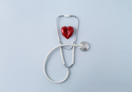 White stethoscope and red polydiagonal decorative heart on pastel background. Medical banner. Doctor's day concept. Selective focus, copy space