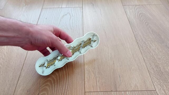 A hand places a disassembled electrical extension cord on a wooden floor, revealing internal components and sockets, illustrating household repair, maintenance, and device structure