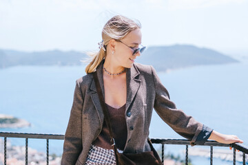 Travel blogger filming live stream on smartphone against mountain coastline, Gen Z female tourist on viewpoint, panoramic sea and hills, social media content creator, sunny outdoor vacation vibe. © shintartanya