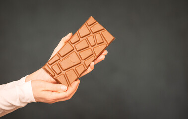 A bar of delicious chocolate in a woman's hand on a dark background