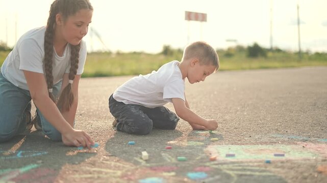 Summer street play chalk unites children. Girl and boy enjoy creating outdoor art. Child starts drawing, kid adds more details. Street fills chalk colors as children turn warm summer into bright art.