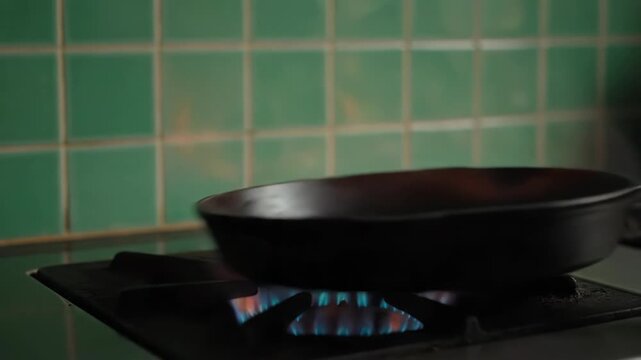A cast iron pan flares with intense flames on a gas stove. The kitchen tile background is a vibrant green.