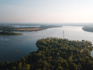 View of a river winding through green trees and hills with a tower in the distance at midday © Ivan Denysenko