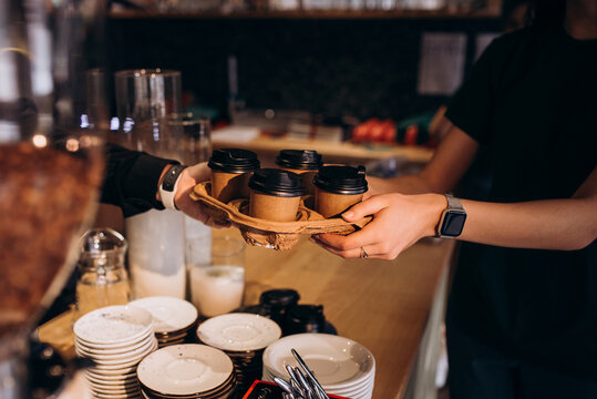 Close up of barista giving takeaway drink carrier with four cups to customer. Coffee to go service concept in cafe setting.