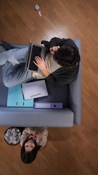 Vertical video stressed mother multi tasking and trying to work from home on a laptop while her playful child distracts her from below, representing the struggles of balancing family and remote work