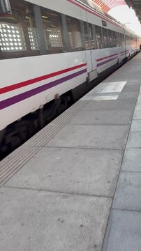 Plano lateral de tren de pasajeros de cercan&iacute;as pasando por una estaci&oacute;n.