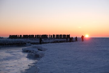 Obraz premium Gdynia, Poland - Frozen Baltic Sea beach with wooden poles and silhouettes of people in Babie Doły in sunrise scenery.