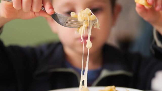 Slow motion 180 fps close-up of a boy lifting a fork with cheese pasta until the threads break - Cinematic lifestyle background of a child enjoying a meal with stretching melted cheese