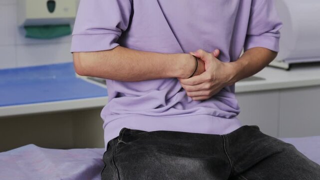 Young man holding flank in pain, possible kidney stones 4k video. pyelonephritis, urinary tract infection during urology consultation.