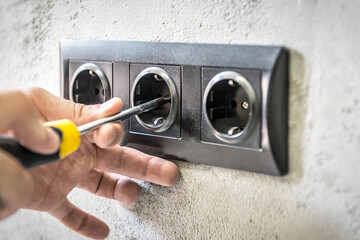 Installation of new black sockets on the wall. Worker installing the power outlet with screwdriver