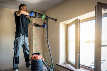 Professional master is installing air conditioner using drill machine making pipe hole during hot season