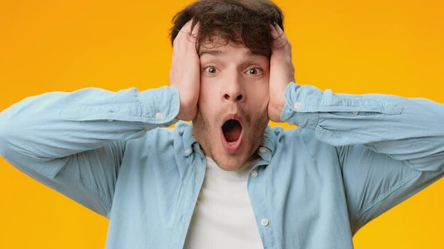 A man shows a surprised expression with hands on his head. He stands against a bright yellow background. The video captures his reaction clearly and vividly.
