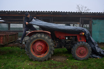 Obraz premium Man covering tractor with protective tarp