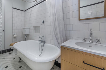 Fototapeta premium This bathroom features a freestanding bathtub, a sink with a wooden cabinet, and a tiled floor. Light fills the space through a window, creating an inviting atmosphere for daily routines