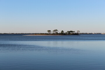 Fototapeta premium Small Tree‑Covered Island on Calm Blue Water