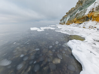 Scenic winter landscape of Estonian limestone cliff coastline with pancake ice formations on the Baltic Sea under a cloudy sky