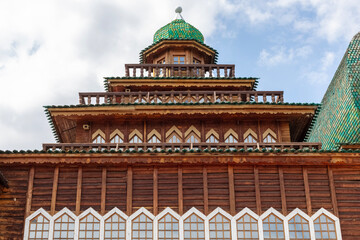 Fototapeta premium A tall wooden structure features a green roof and many windows. It stands in a park under a blue sky with some clouds. Visitors enjoy the area around the building.