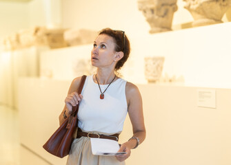 Obraz premium Adult woman with brochure looking at antique exhibit in museum hall..