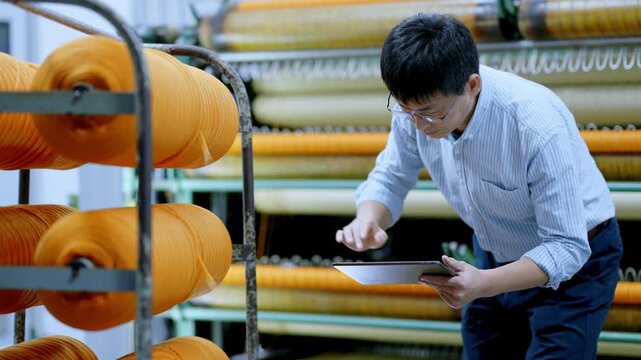 Factory worker inspecting orange yarn spools in a textile manufacturing facility