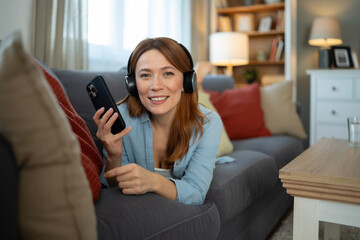 Obraz premium Woman relaxing at home enjoying music using smartphone