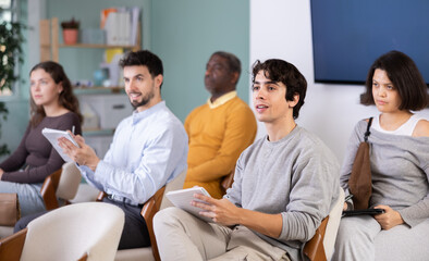 Fototapeta premium In lecture meeting, young man listen to teacher, write down summary. Language courses, exam preparation, lecture and practical classes at school. Students taking trial class in language courses