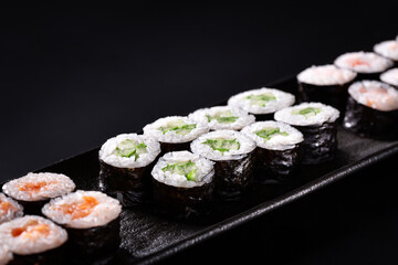 Sushi maki roll set with cucumber, shrimp and salmon on black plate. Closeup on dark background