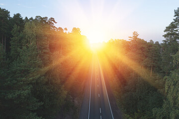 Aerial view from drone on asphalt road through the forest at sunset time