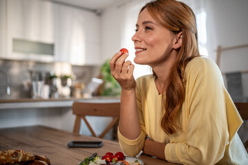 Woman enjoying healthy snack with cherry tomato in kitchen